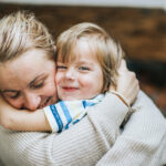 Happy mother embracing her small son at home, while boy is looking at camera.