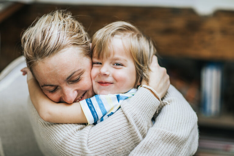 Happy mother embracing her small son at home, while boy is looking at camera.