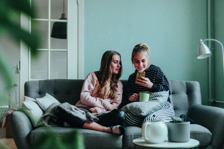 Photo series of two female teenage friends using social media for various purposes at home on the couch.