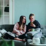 Photo series of two female teenage friends using social media for various purposes at home on the couch.