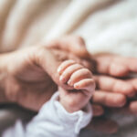 Newborn baby boy laying on bed, mother and father holding his hand