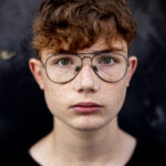 close-up  of red-haired teenage boy with freckles, against a black wall in the street