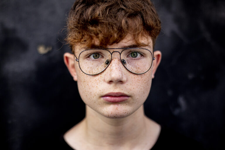 close-up  of red-haired teenage boy with freckles, against a black wall in the street